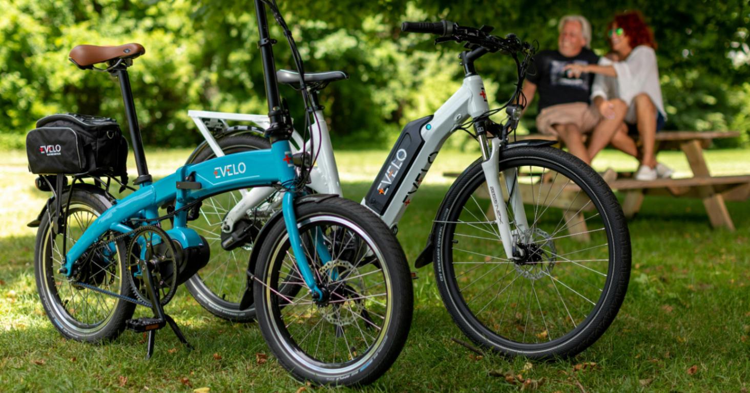E-bike riders sitting on a bench taking a break from cycling Two e-bikes (folding and standard) parked in the foreground with two riders sat on a picnic bench chatting