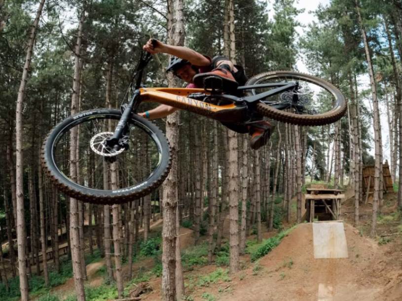 Orange Canyon Spectral downhill e-mountain bike in flight with large wooden ramp in the background