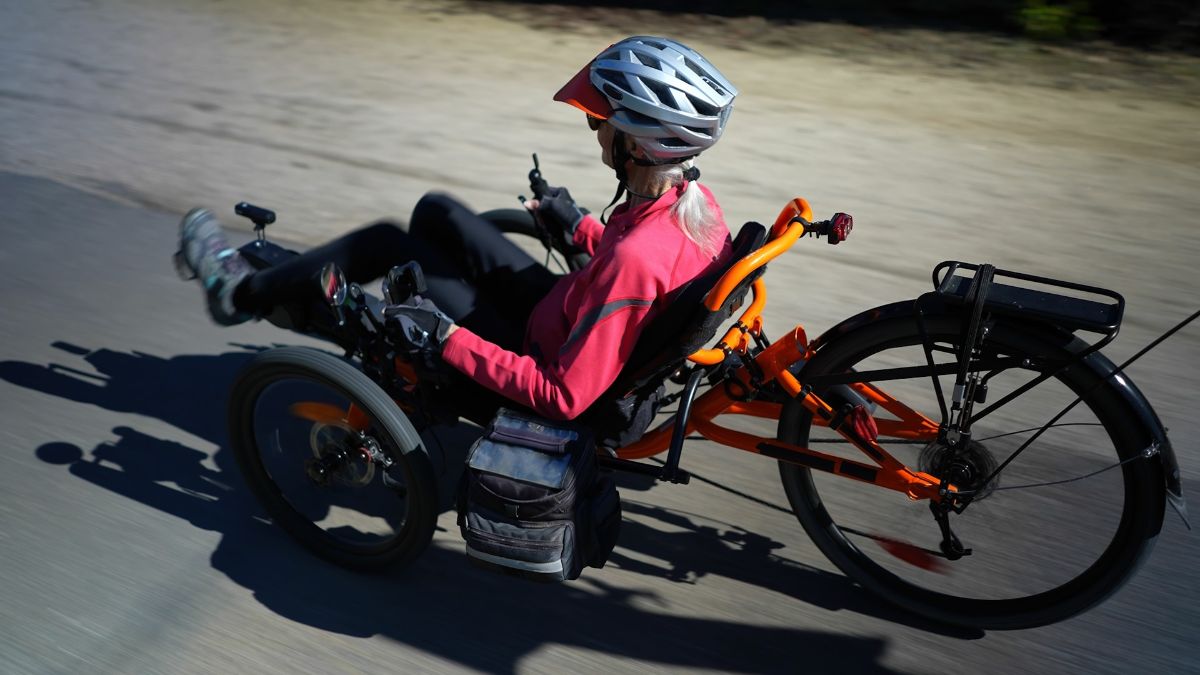 Women riding an orange recumbent electric bike with mudguards and a rear rack