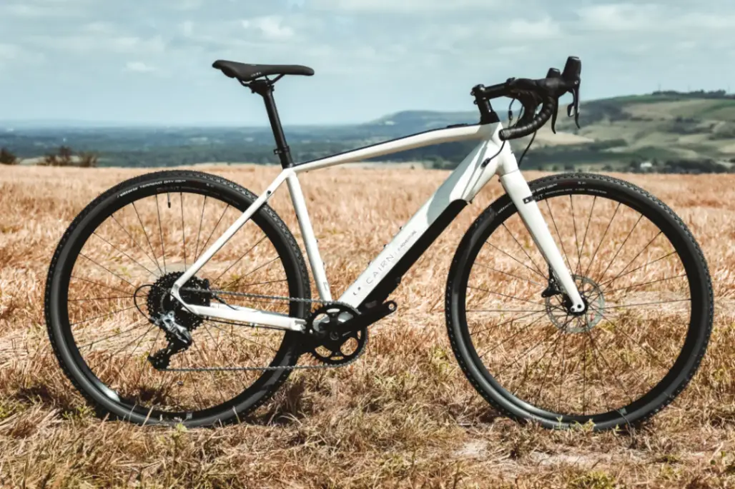 White electric gravel bike photographed in a sunny corn field with green countryside in the background
